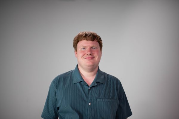 Headshot of Elliot Dennis in a teal shirt, smiling at the camera.